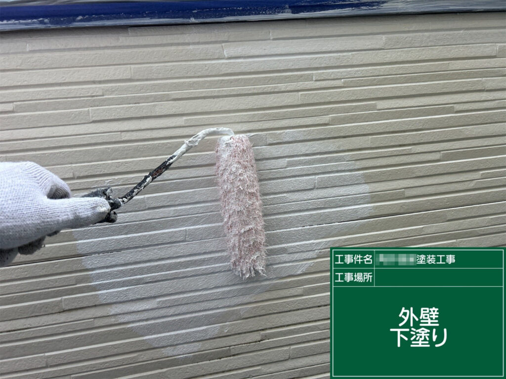 外壁に下塗り材を塗布している様子です。上塗り塗料の密着を高め、塗装の耐久性を左右する重要な工程で、外壁材に合わせた最適な下塗りが行われています。